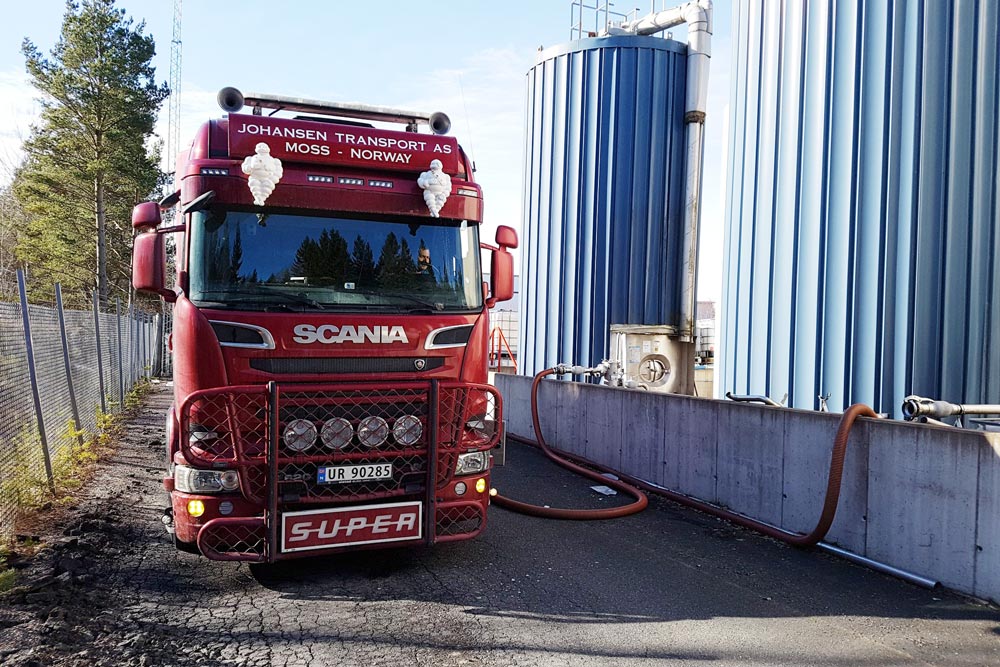 Röd lastbil med norsk registreringsplåt fyller på glykol i behållare