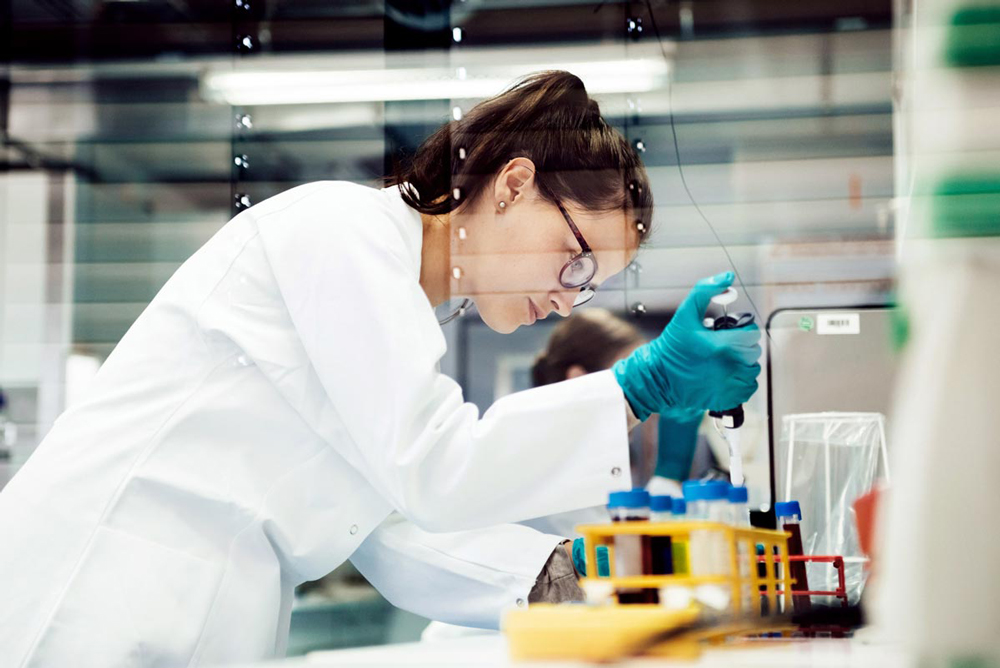 Kvinnlig forskare använder pipett för att flytta lösning från ett provrör till ett annat i labb